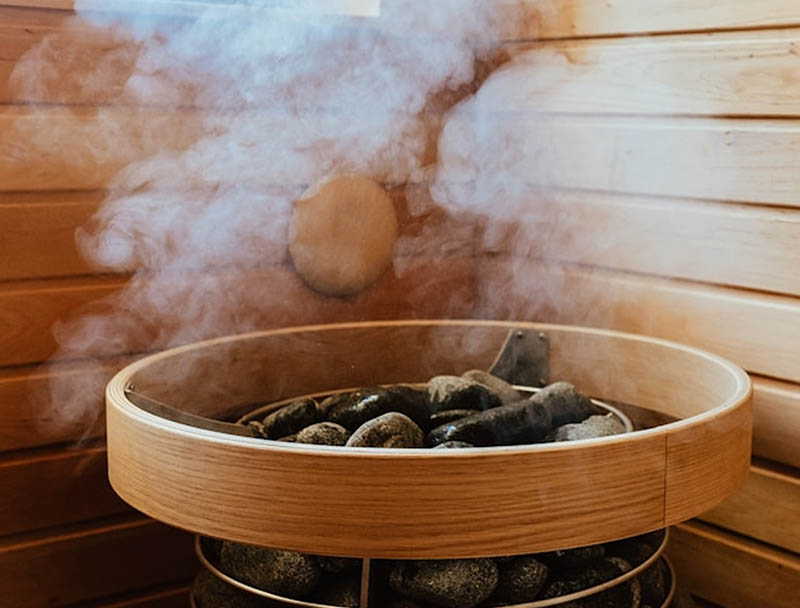 Des pierres chaudes fumantes dans un poêle à sauna en bois dégagent une vapeur intense et apaisante. Des pierres chaudes fumantes dans un poêle à sauna en bois dégagent une vapeur intense et apaisante.