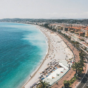 Une longue plage de galets bordée par une mer turquoise longe la Promenade des Anglais.