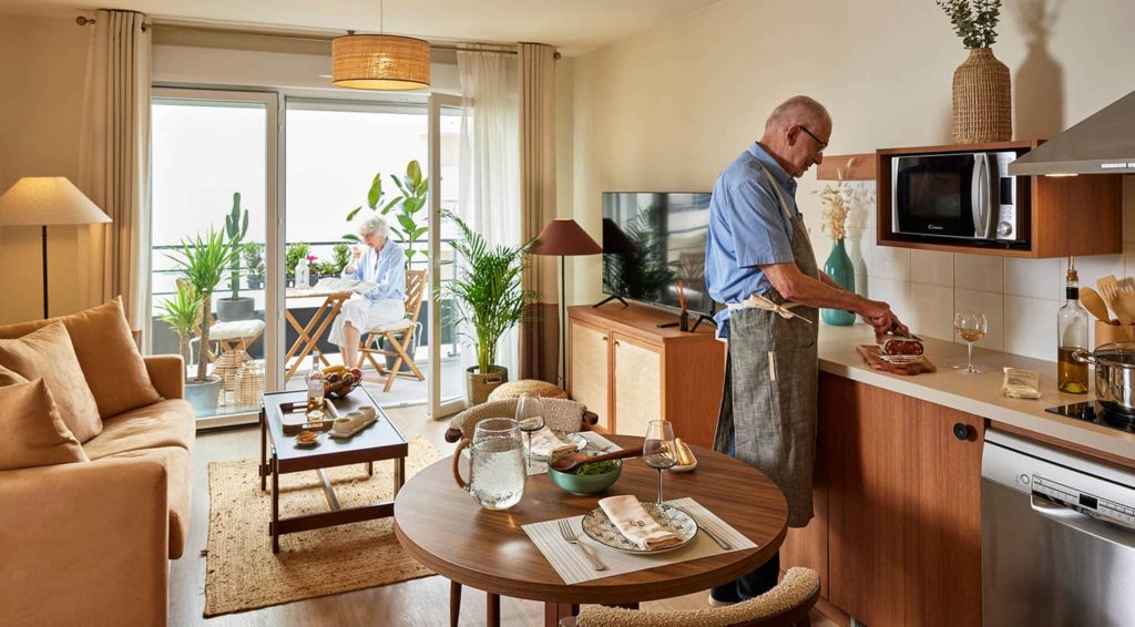 Cuisine équipée chaleureuse où un senior prépare tranquillement son repas, entre indépendance et convivialité. Cuisine équipée chaleureuse où un senior prépare tranquillement son repas, entre indépendance et convivialité.