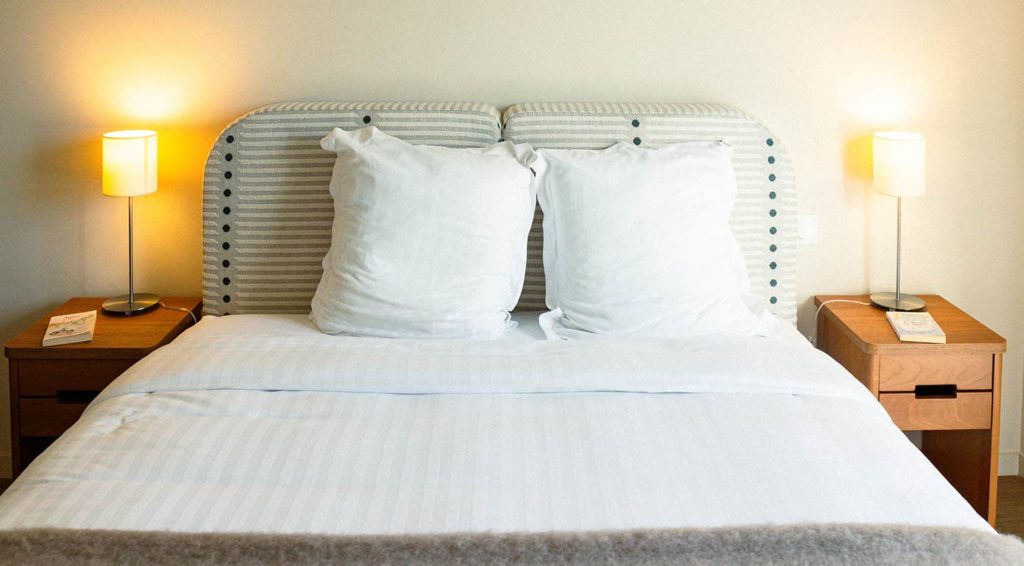 Chambre douce et raffinée avec tête de lit rayée, linge blanc immaculé et chevets chaleureux. Chambre douce et raffinée avec tête de lit rayée, linge blanc immaculé et chevets chaleureux.
