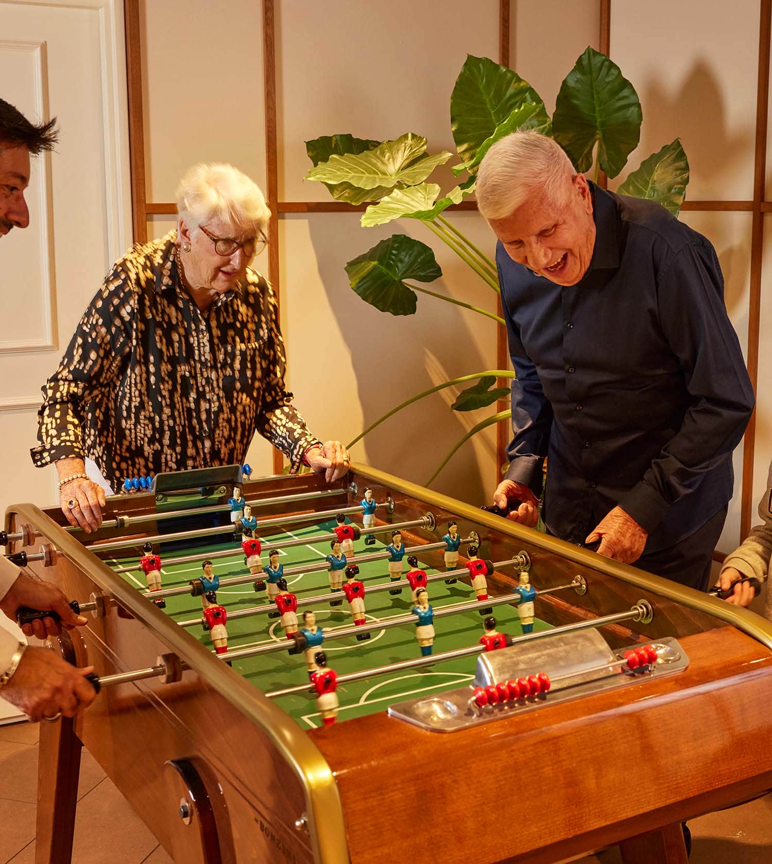 Deux résidents seniors jouent ensemble au baby-foot dans une pièce chaleureuse en bois. Deux résidents seniors jouent ensemble au baby-foot dans une pièce chaleureuse en bois.